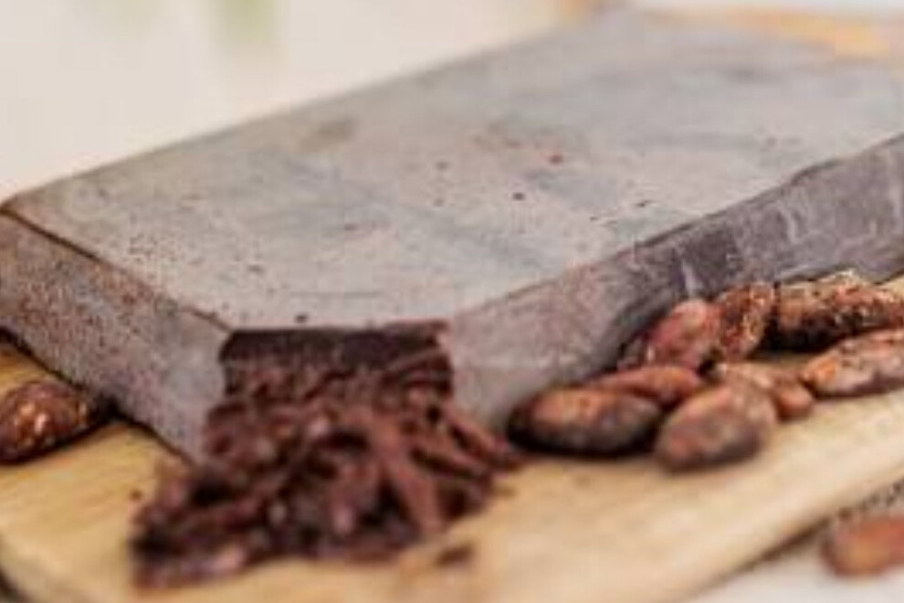 Raw cacao nibs and whole beans beside a stone grinding slab