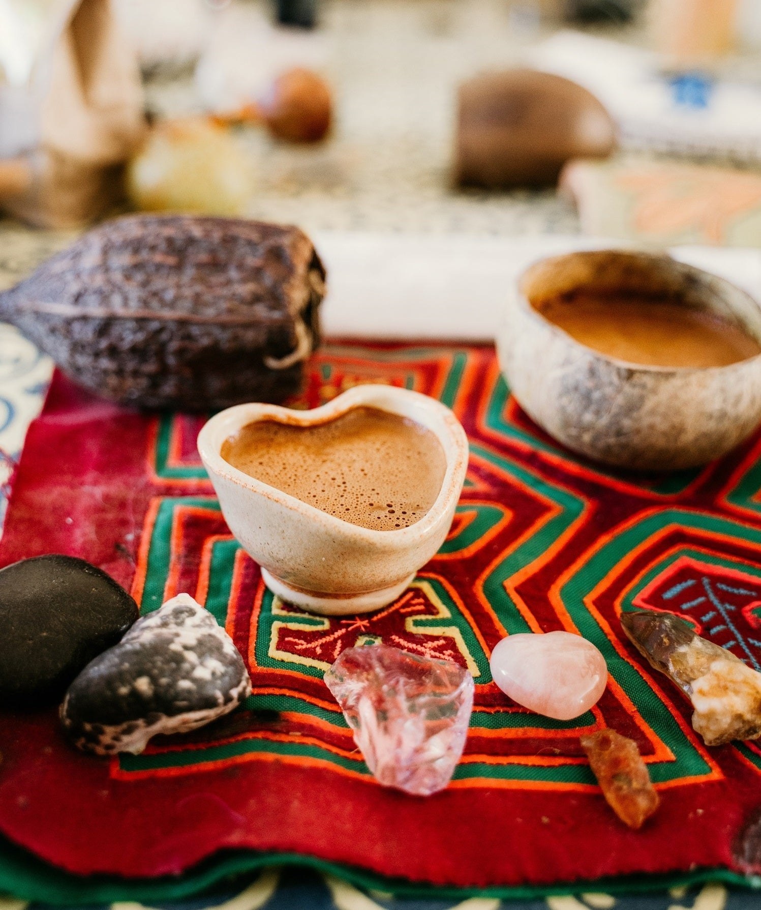 A heart-shaped cup of prepared cacao beside a cacao pod and ceremony stones